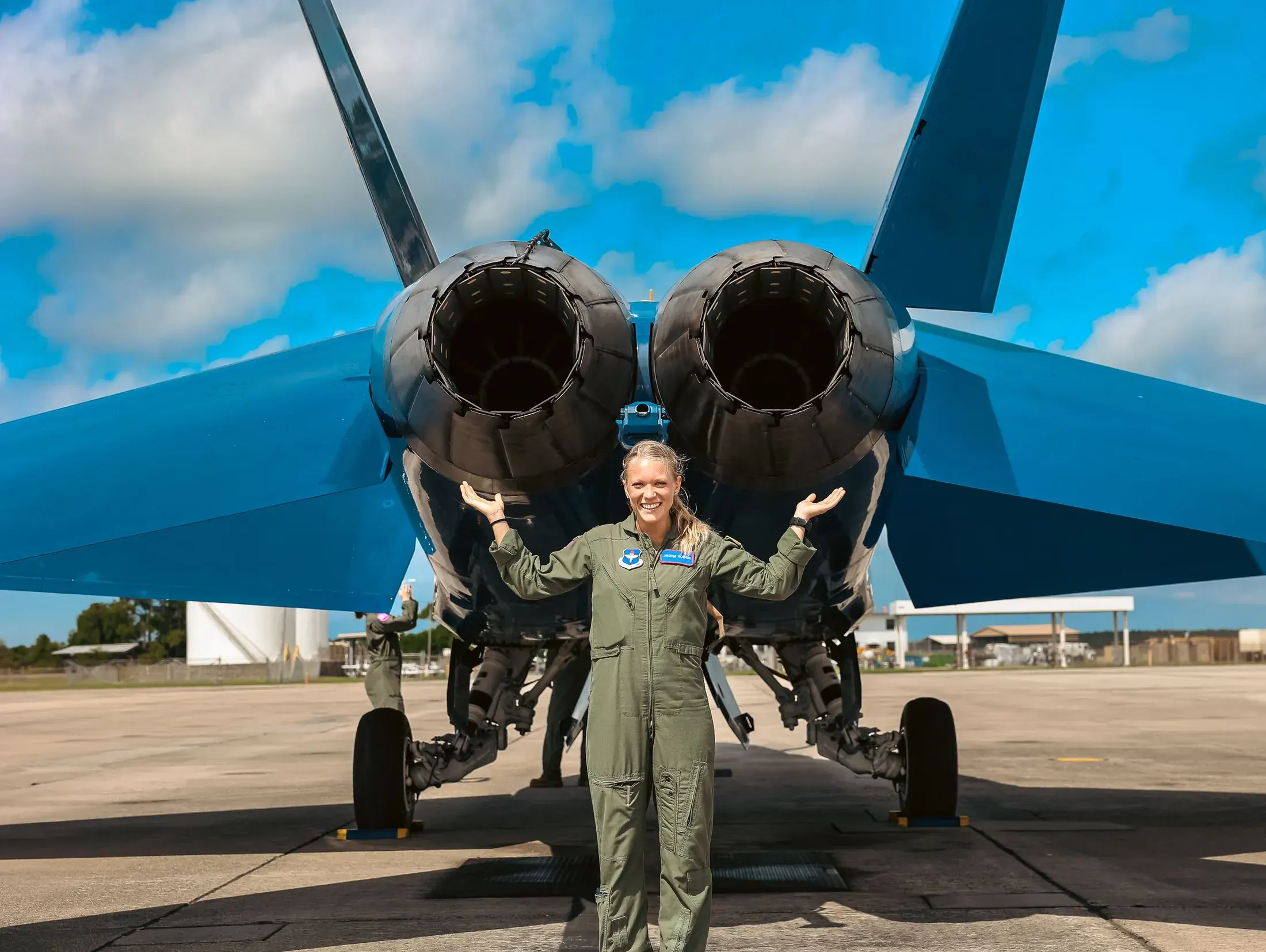 Aviator standing beneath the engines of a blue fighter jet