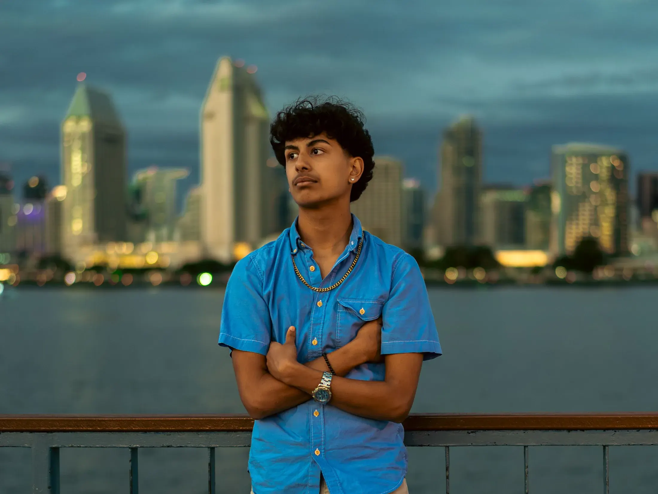 Young man in a blue shirt with the San Diego skyline at dusk