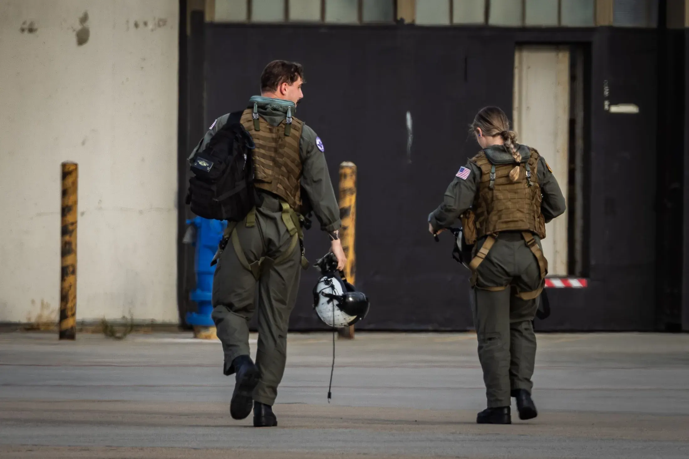 Two service members in gear walking toward a hangar