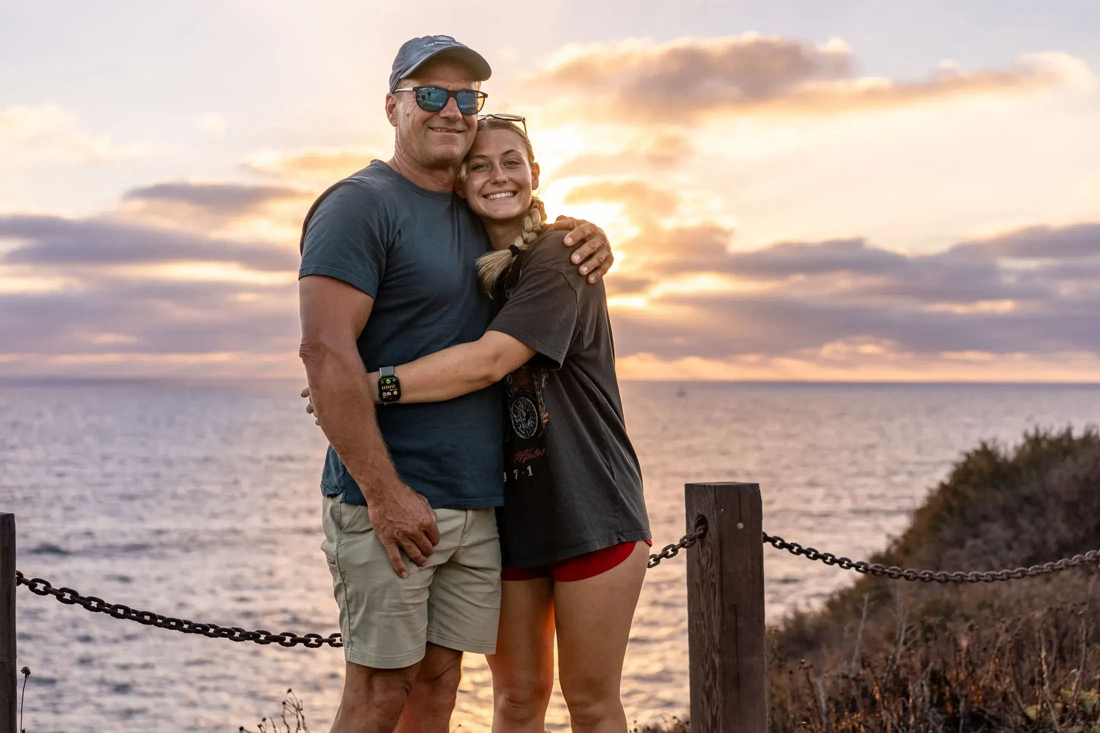 Couple hugging on a bluff above the ocean at sunset