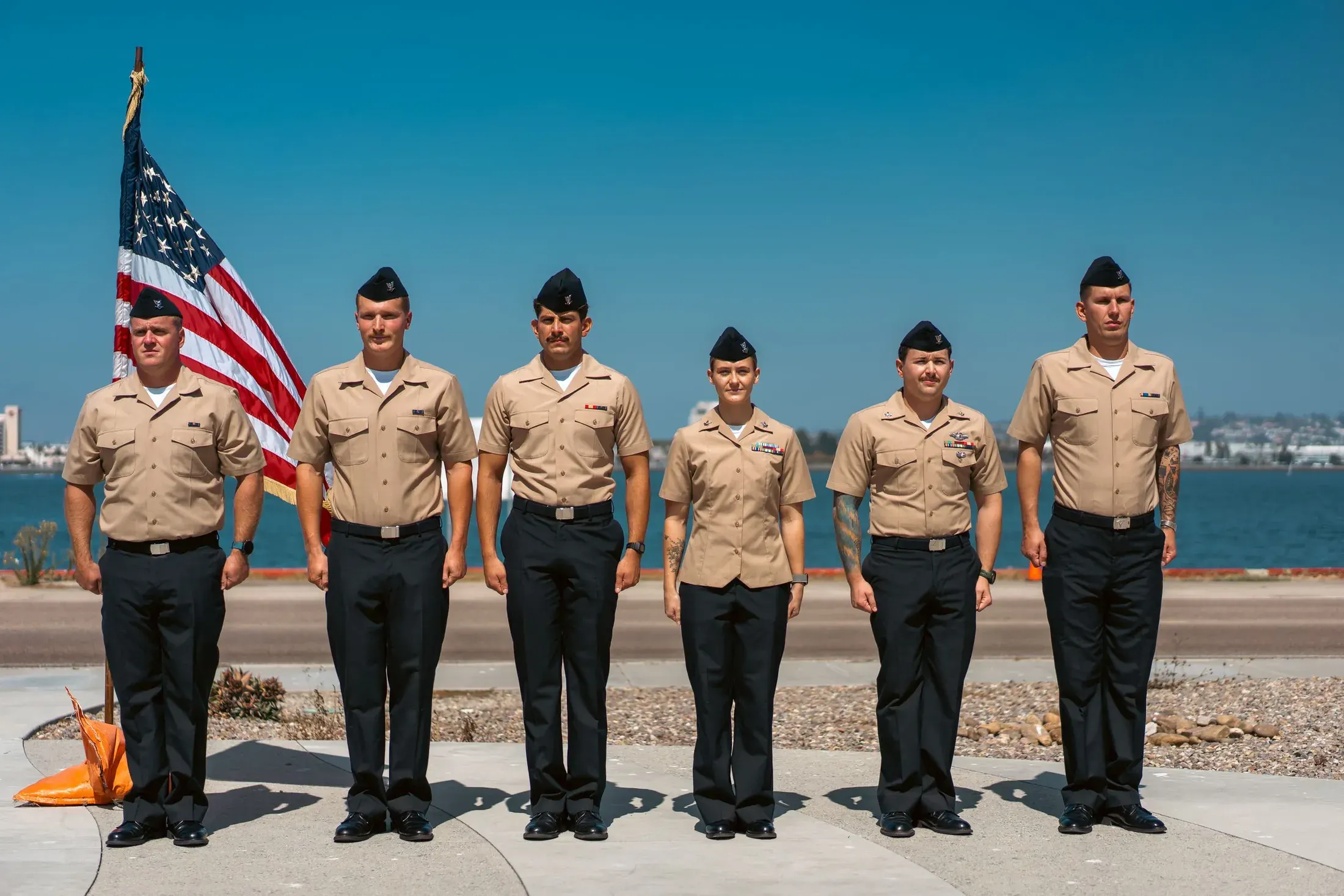 Row of sailors in khakis in front of an American flag