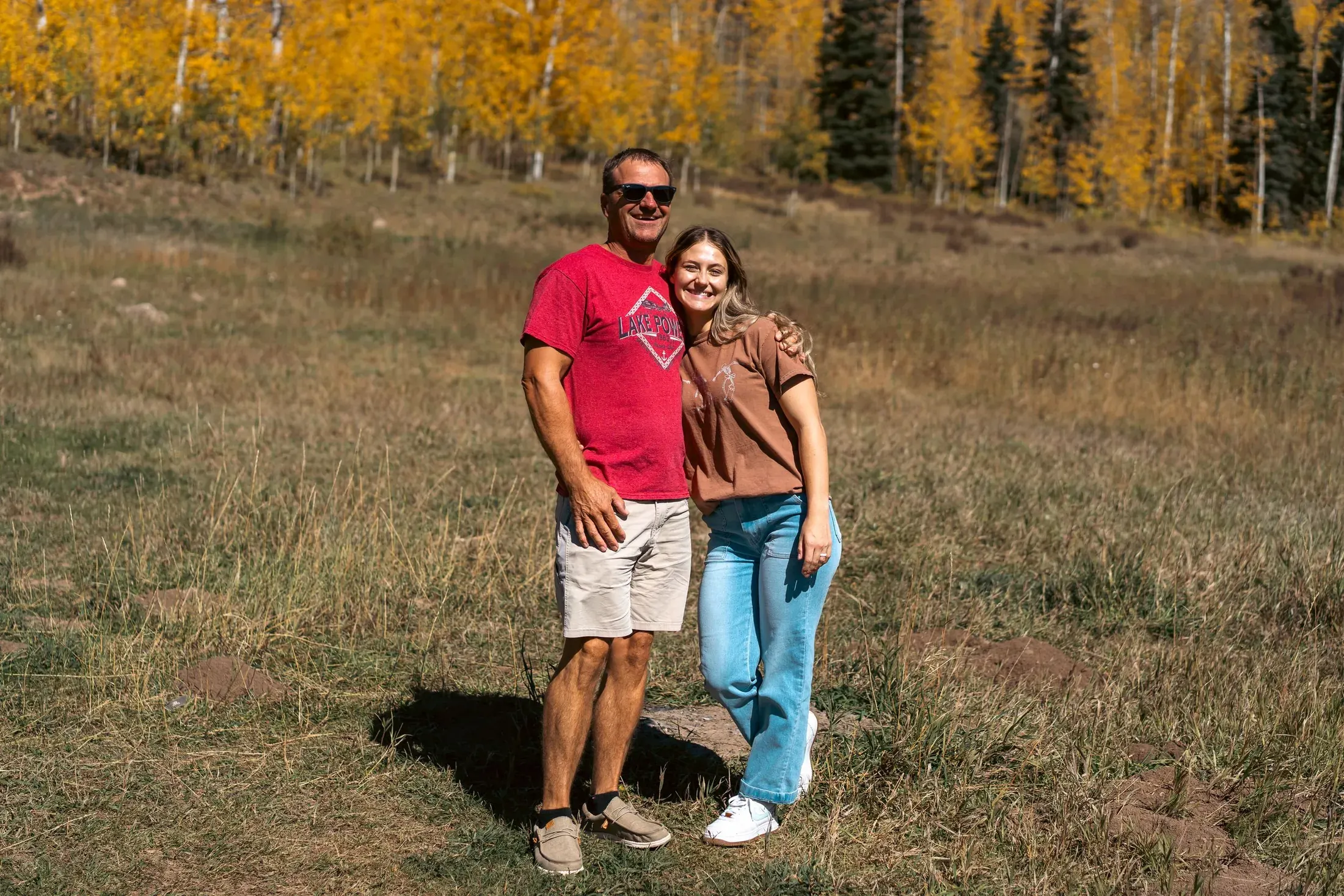 Couple in a meadow with golden aspen trees behind them