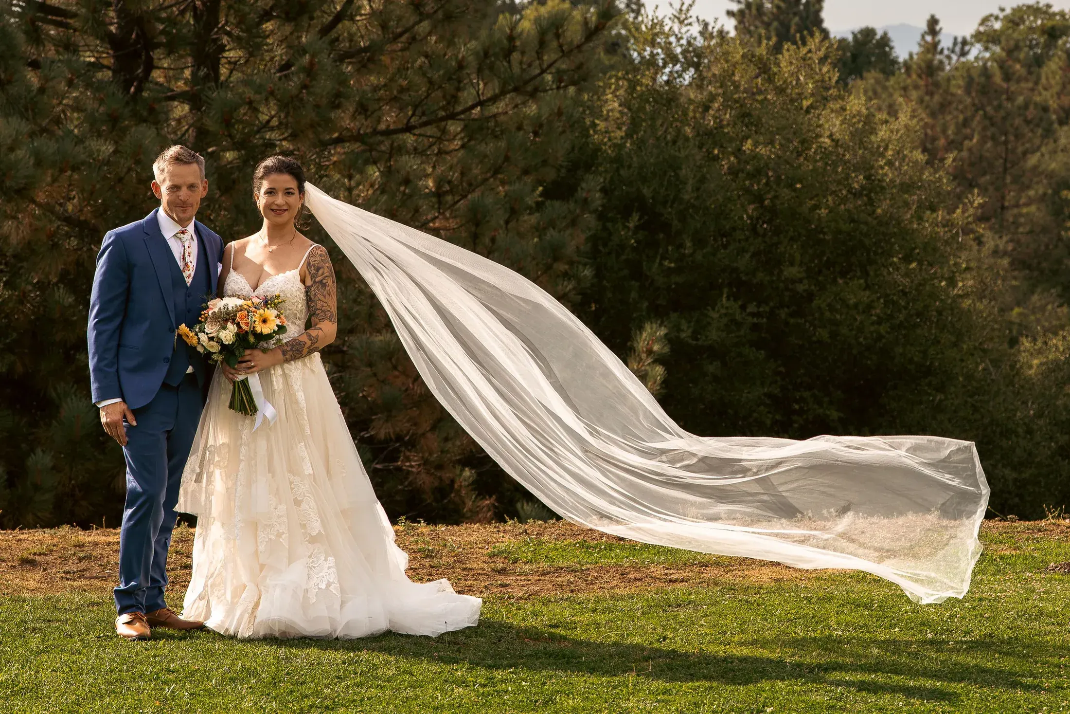 Bride and groom on the lawn as her veil flies in the wind