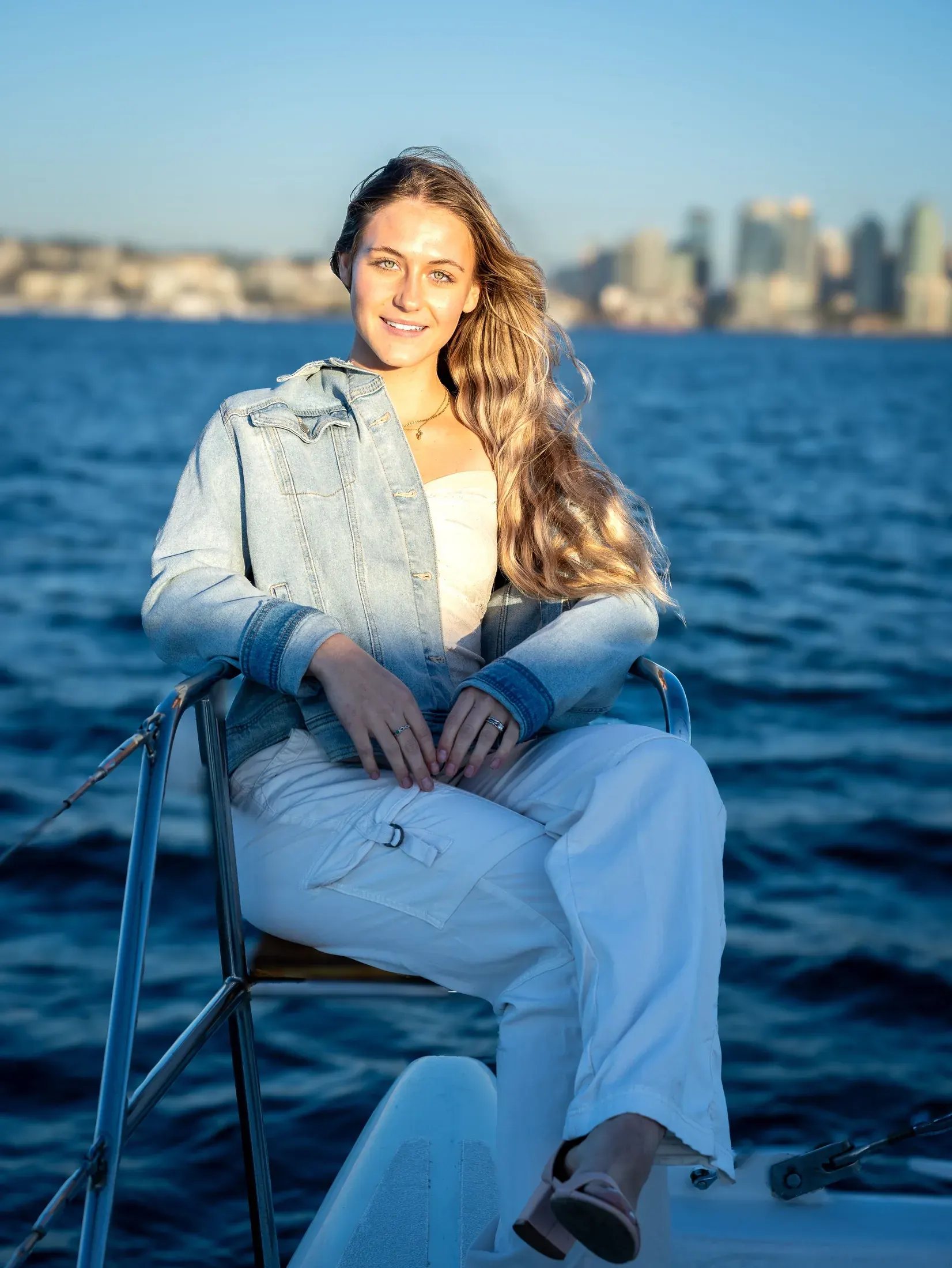 Woman in a denim jacket seated on a boat with the San Diego skyline behind her