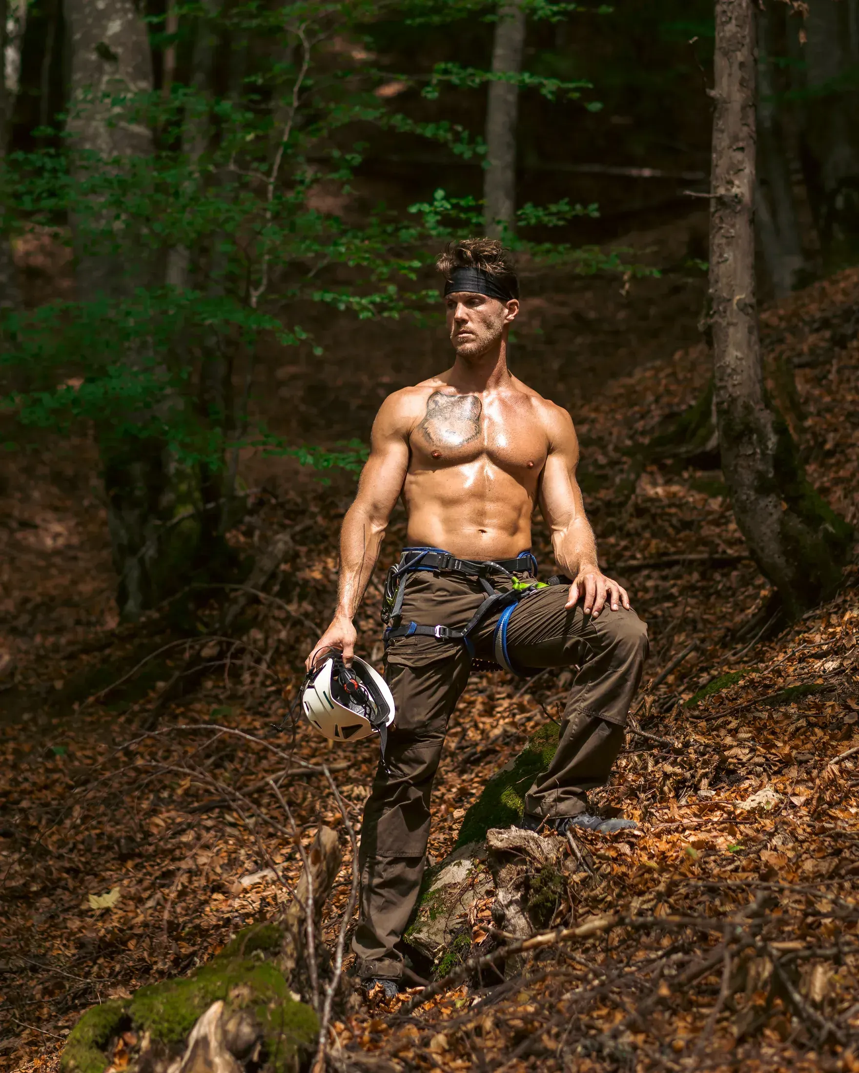 Shirtless man standing in a forest with his shirt over his shoulder