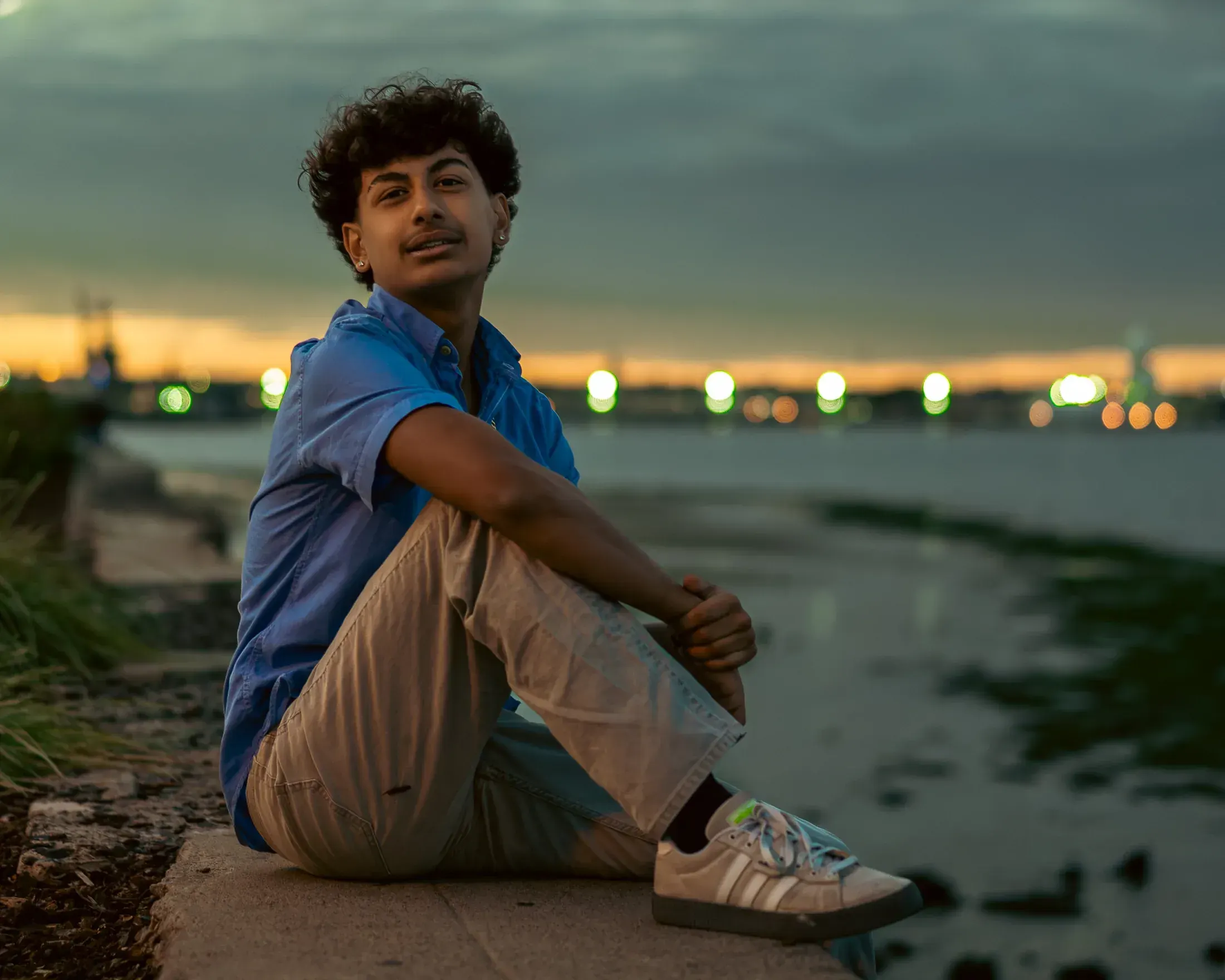 Young man sitting by the bay at dusk with the skyline behind him