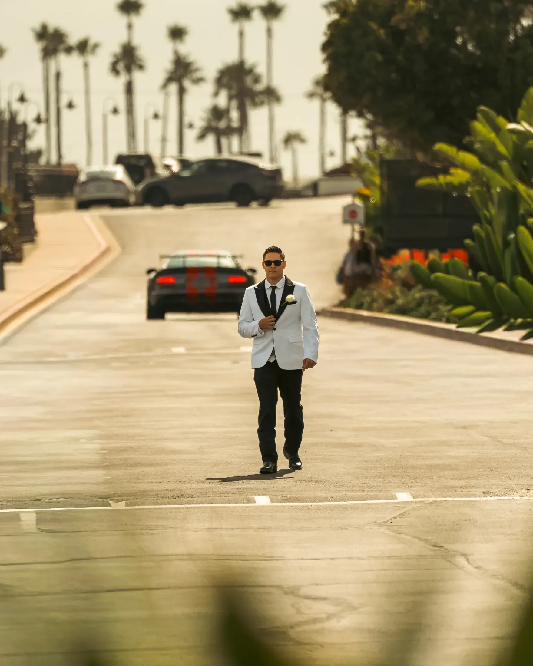 Man in a white jacket walking up a palm lined street