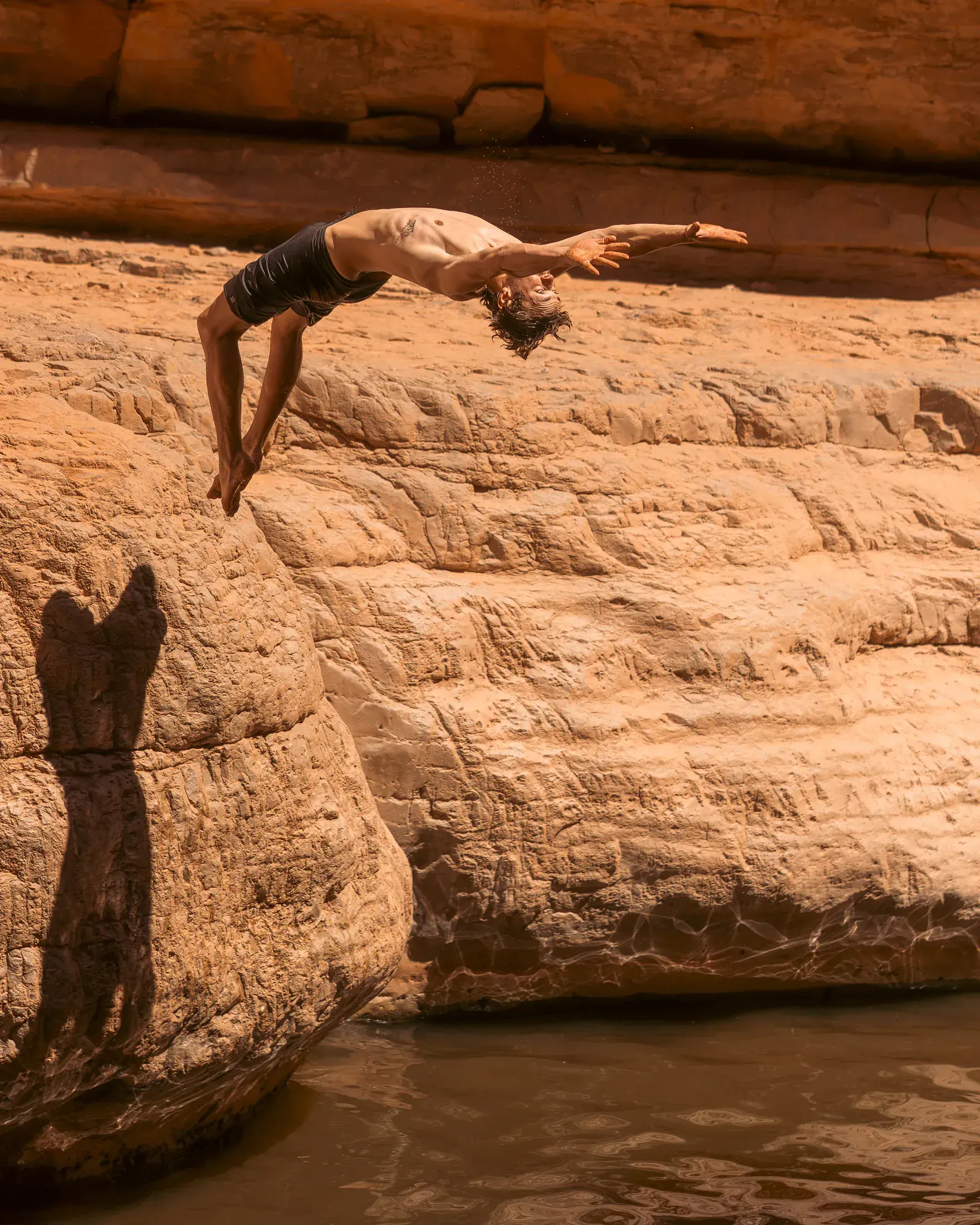 Backflip off a red rock ledge into a swimming hole