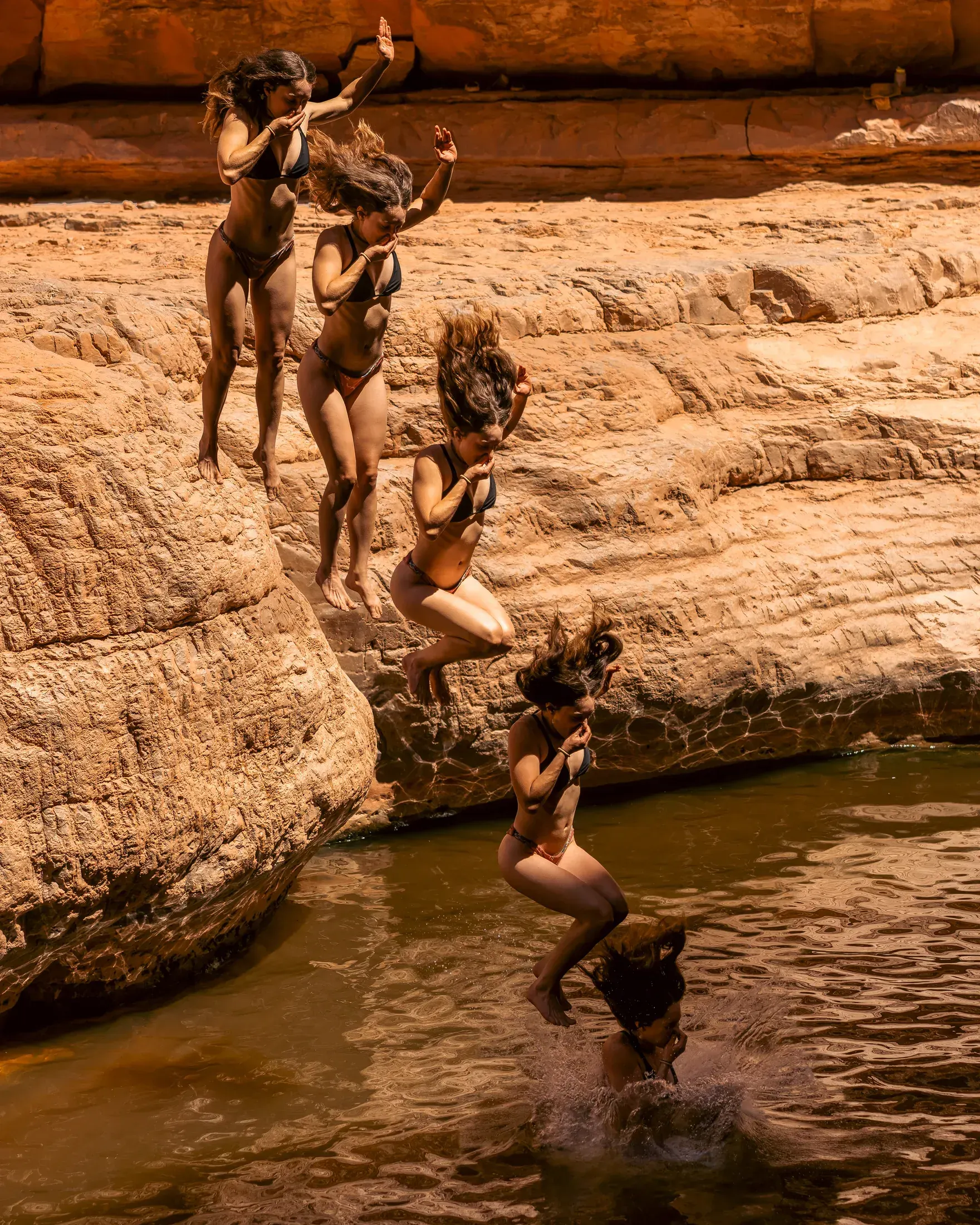 Friends jumping off the rocks into a desert swimming hole