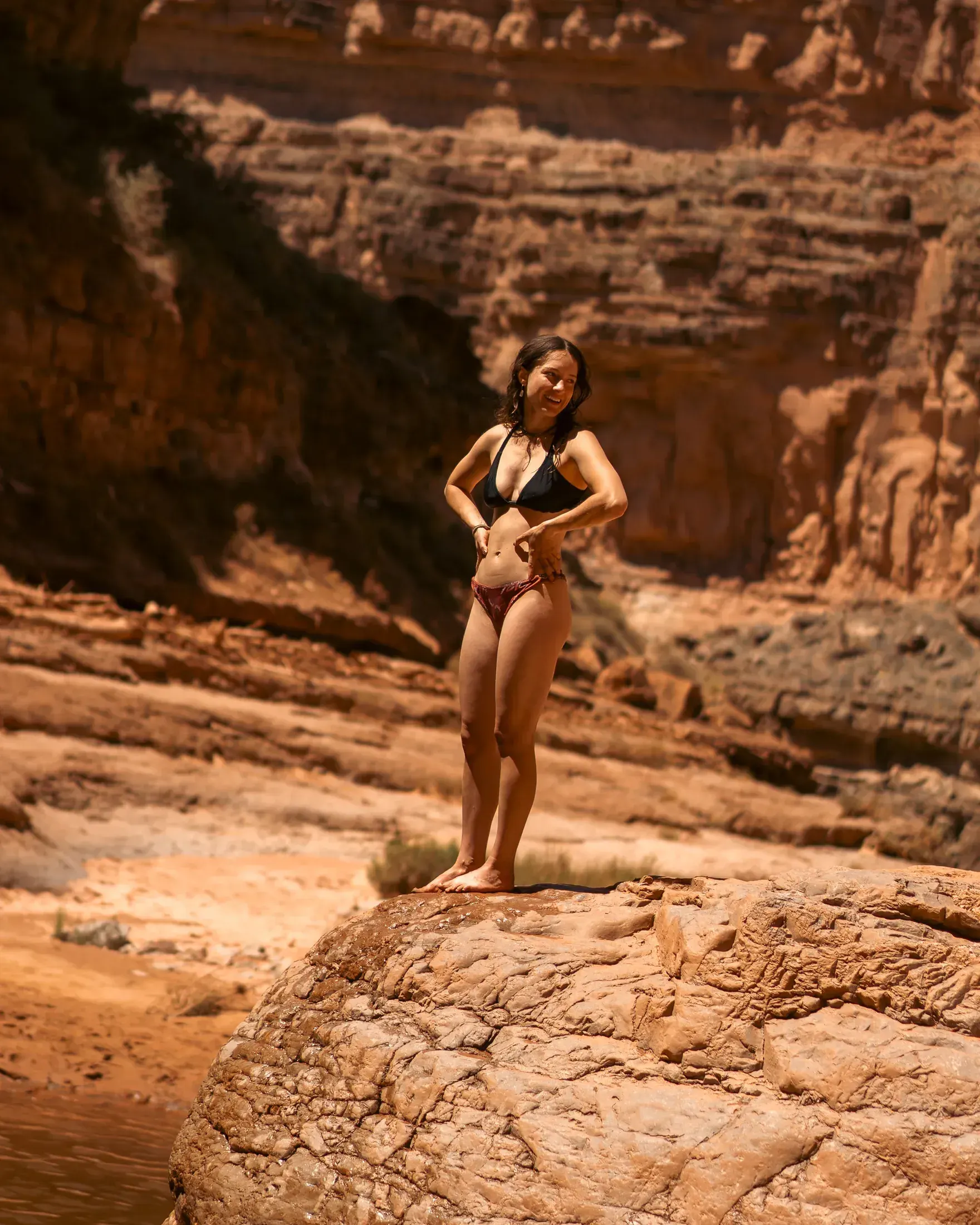 Woman standing on a red rock ledge above the water