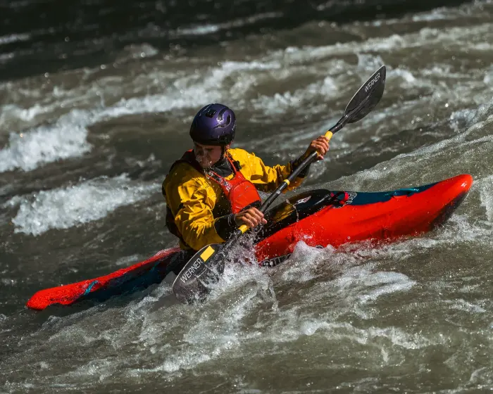 Kayaker in a red boat charging a rapid