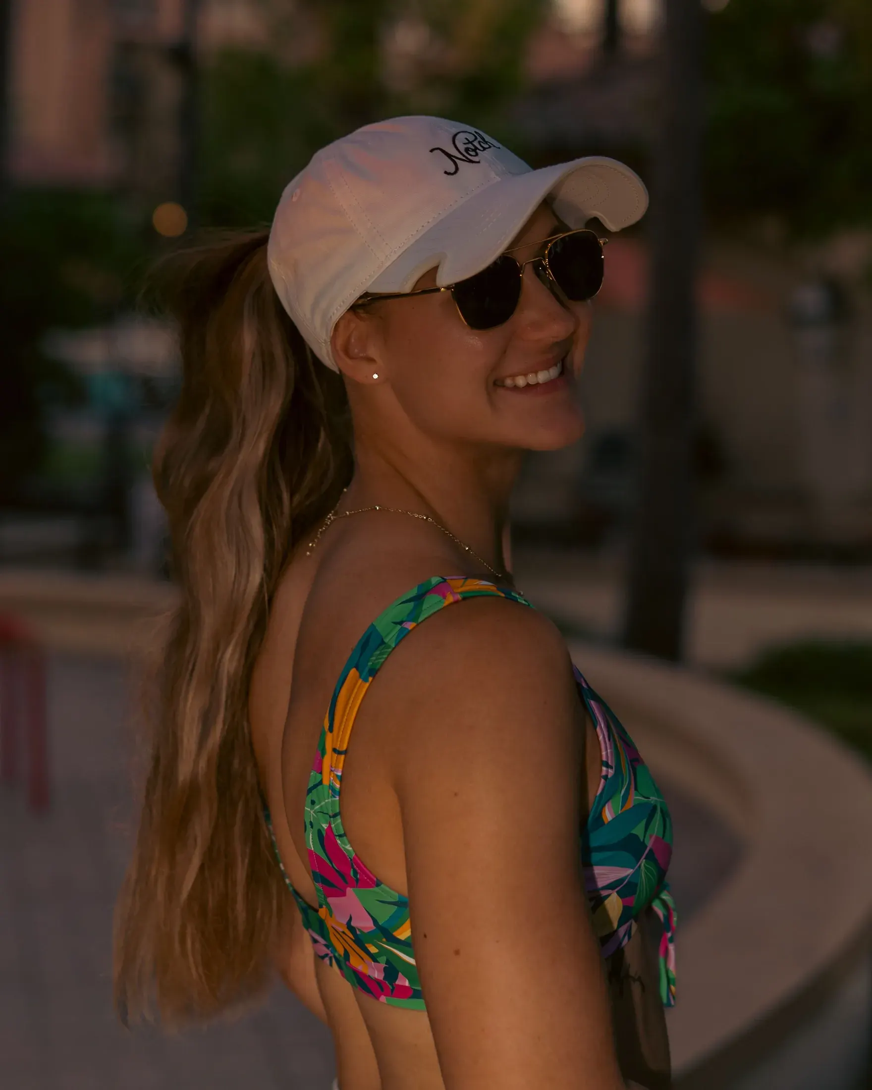 Woman in a white cap and floral swimsuit smiling over her shoulder