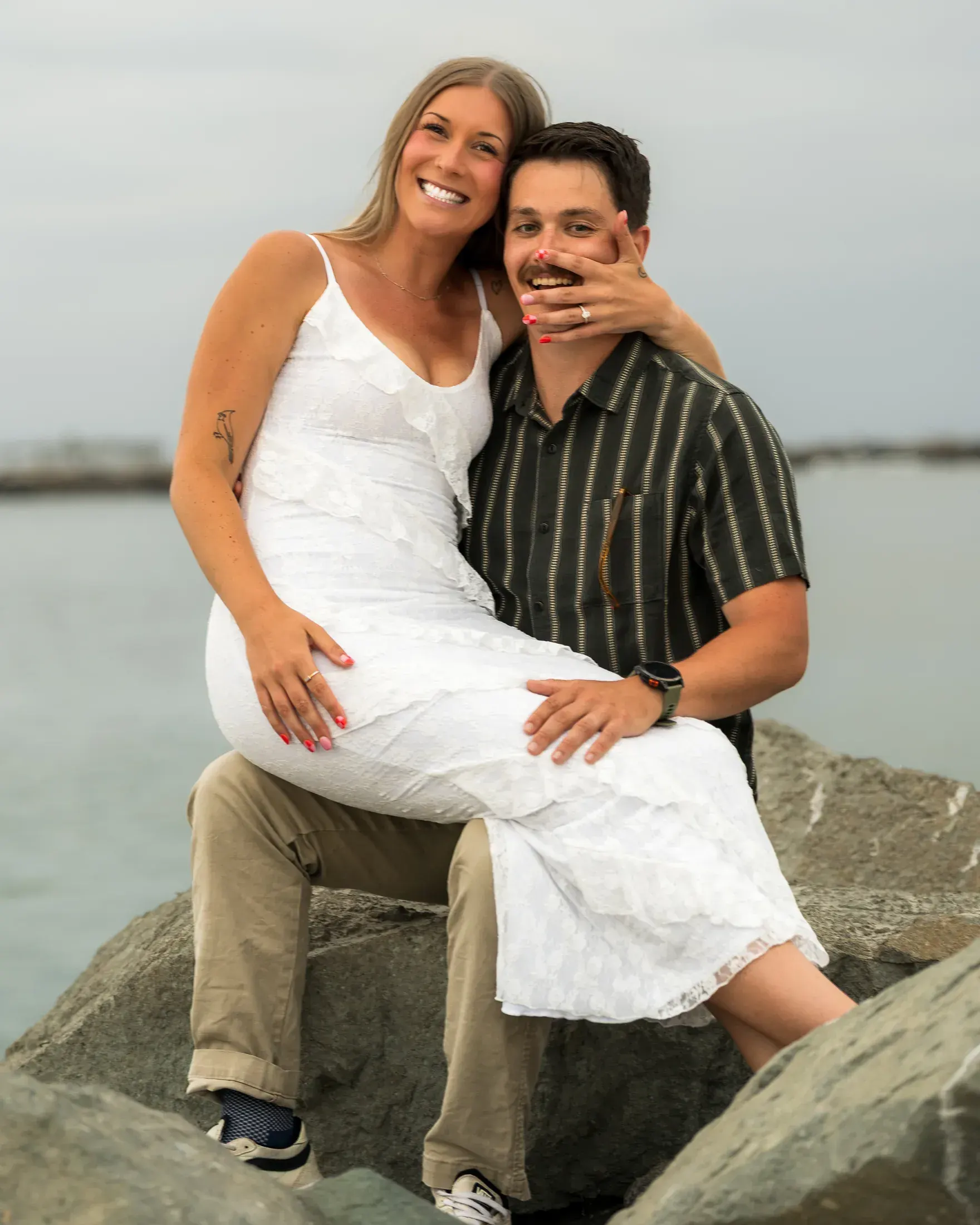 Engaged couple sitting on the rocks by the water