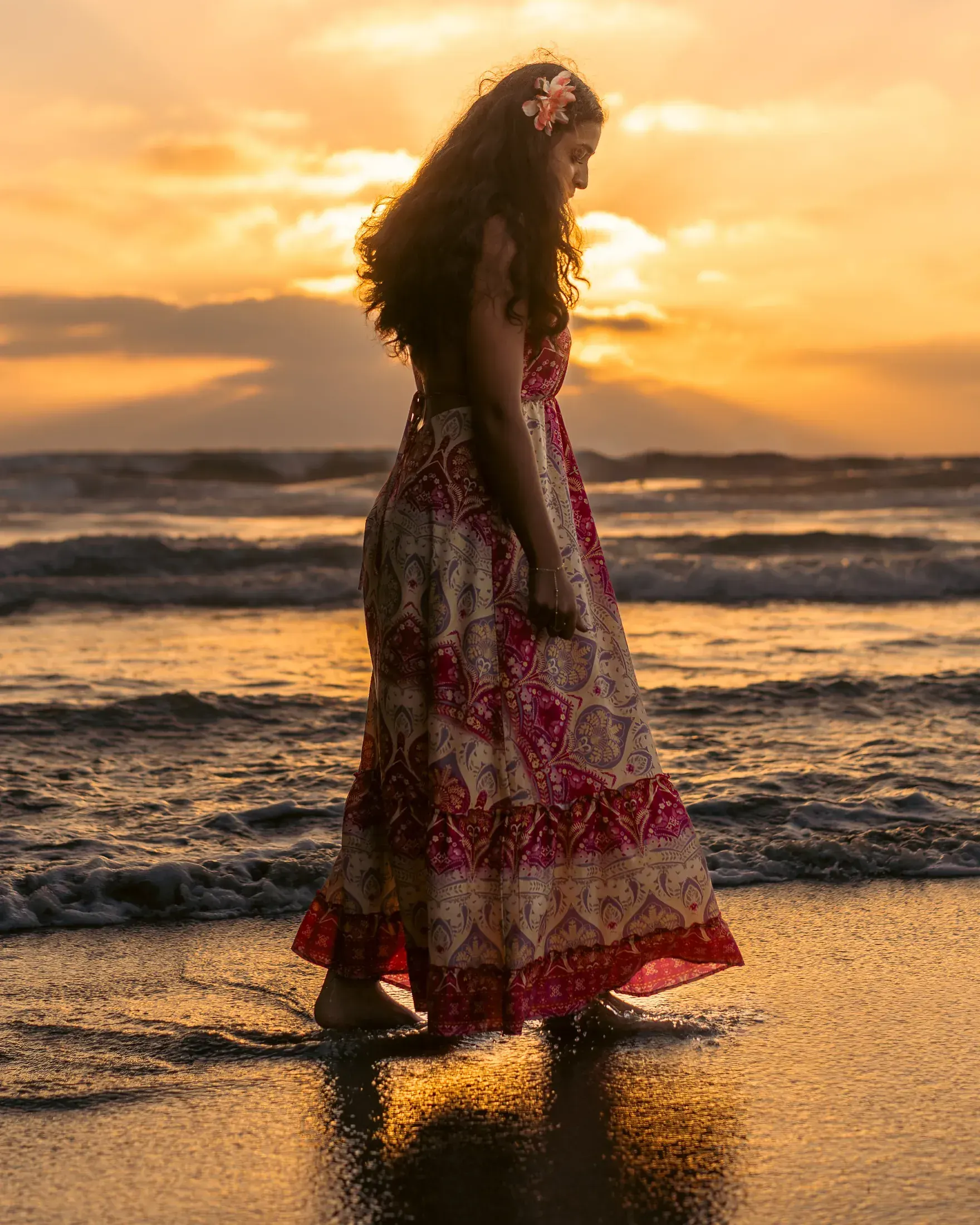 Woman in a flowing dress walking the tide line at sunset