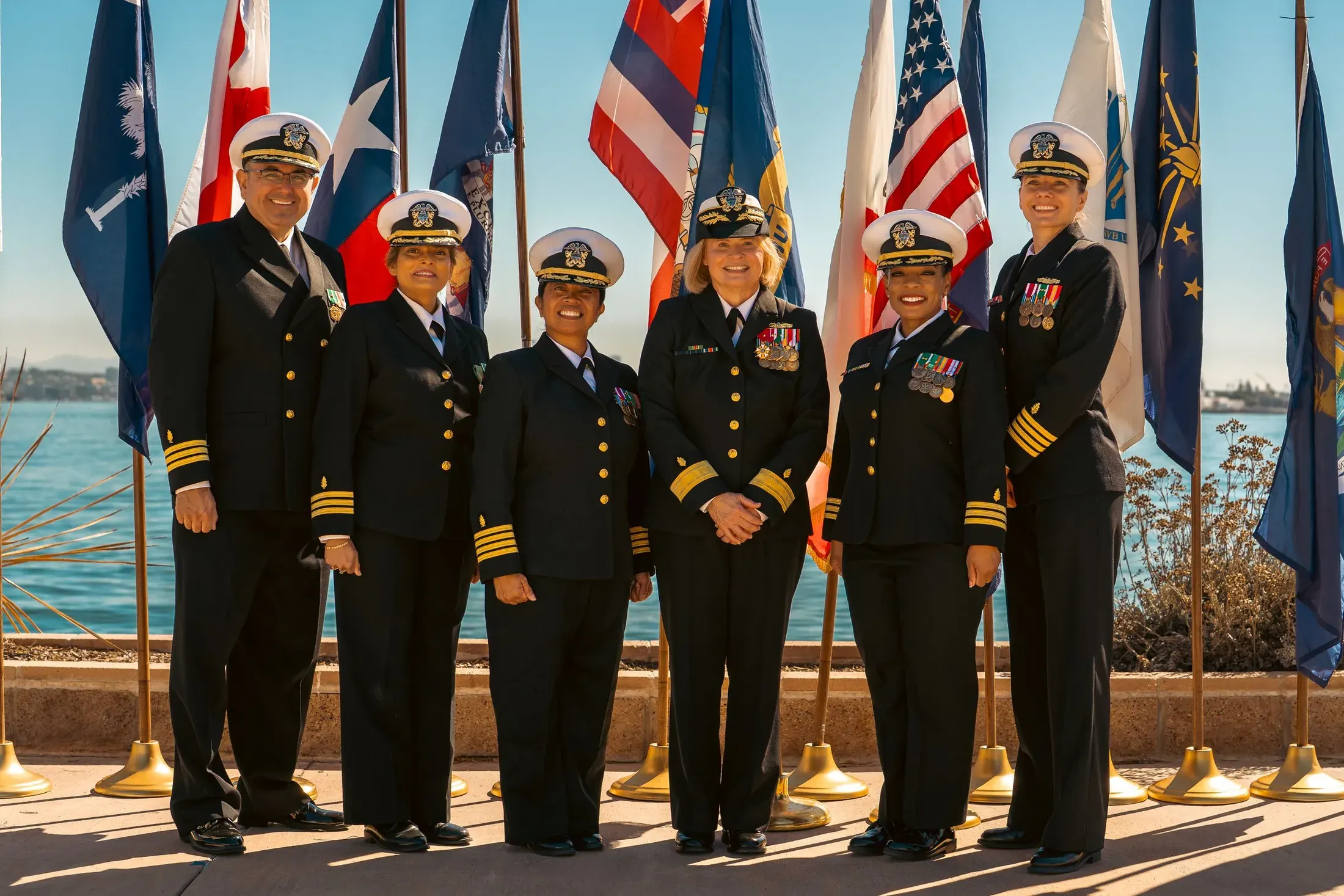 Navy officers in dress blues lined up in front of flags