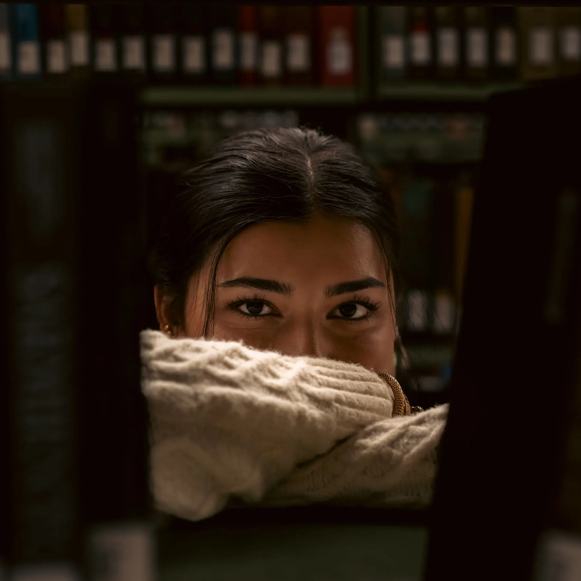 Moody portrait of a woman peeking over a knit sweater
