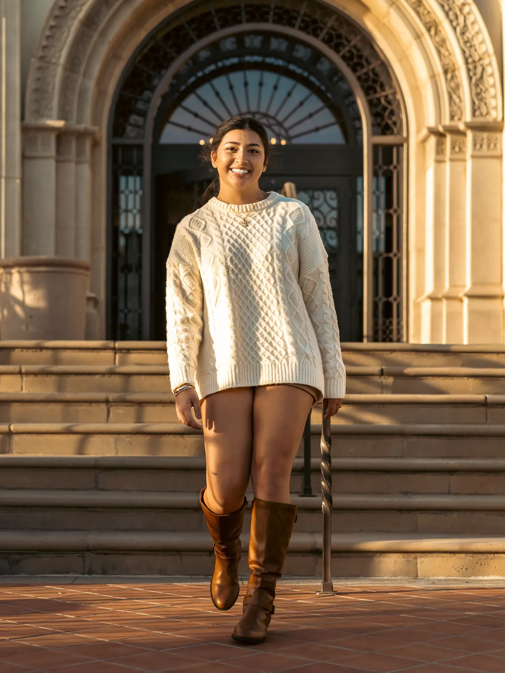 Woman in a cream sweater and boots on the steps of an arched doorway