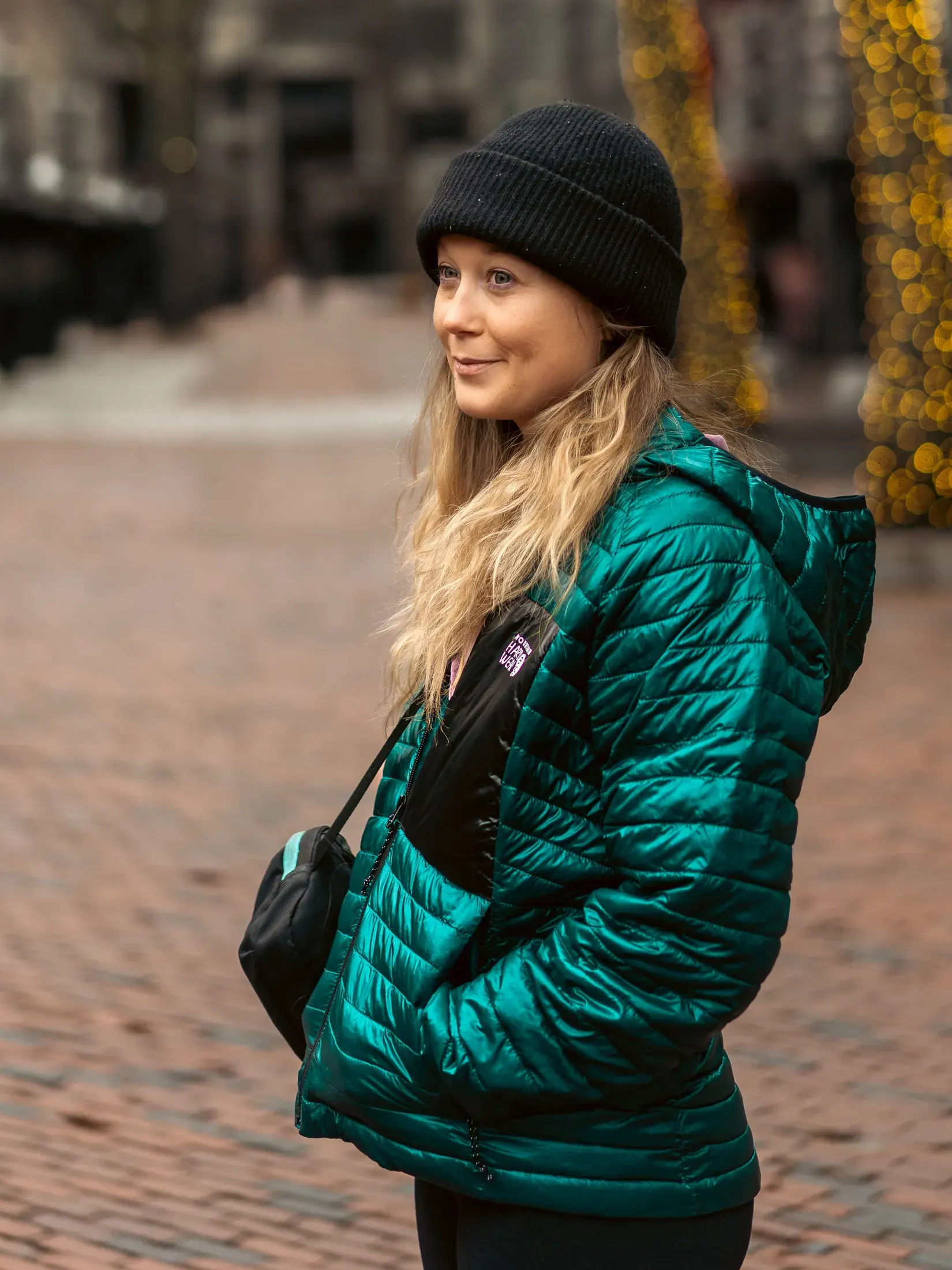 Woman in a beanie and green puffer jacket on a brick walkway