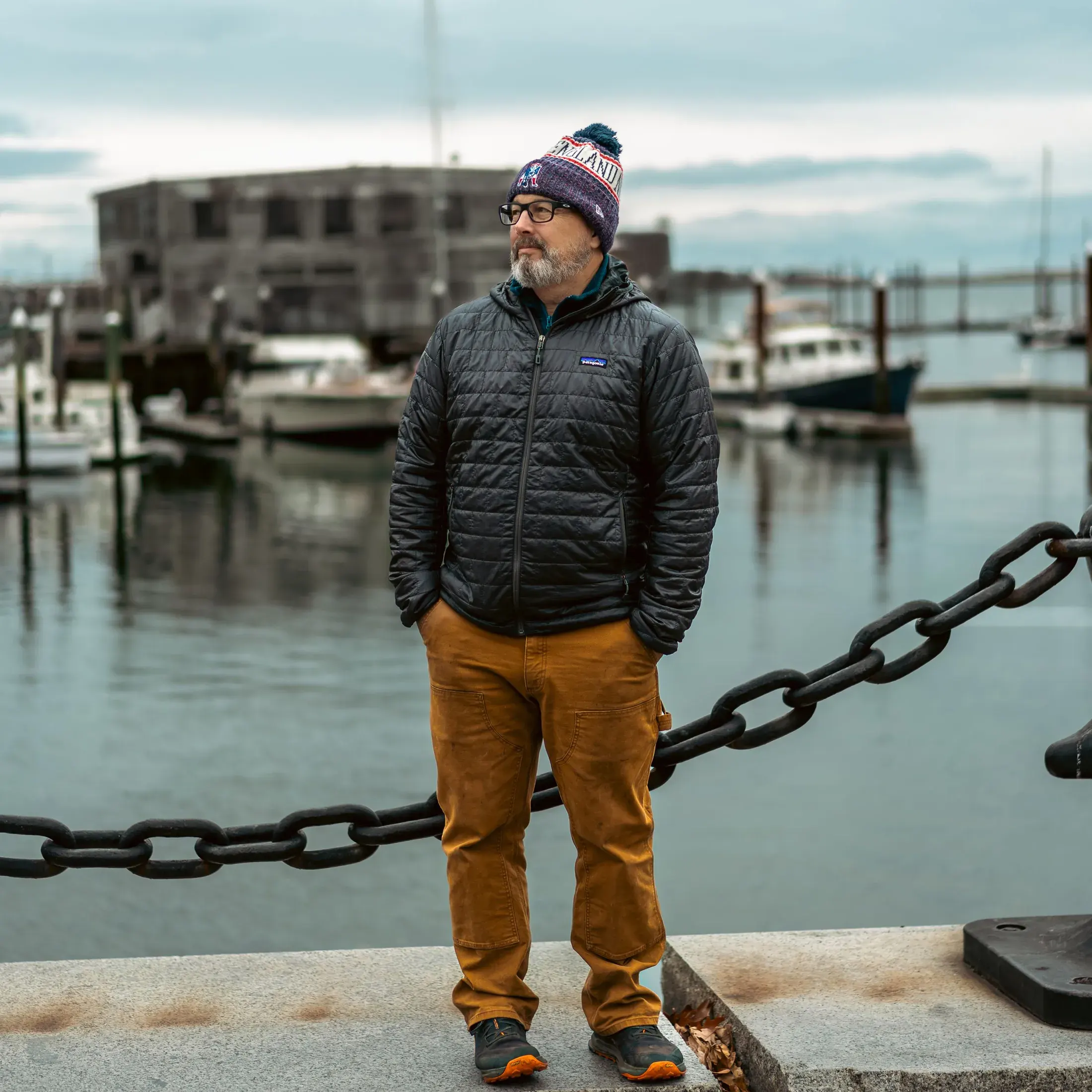 Man in a beanie standing by a harbor chain rail