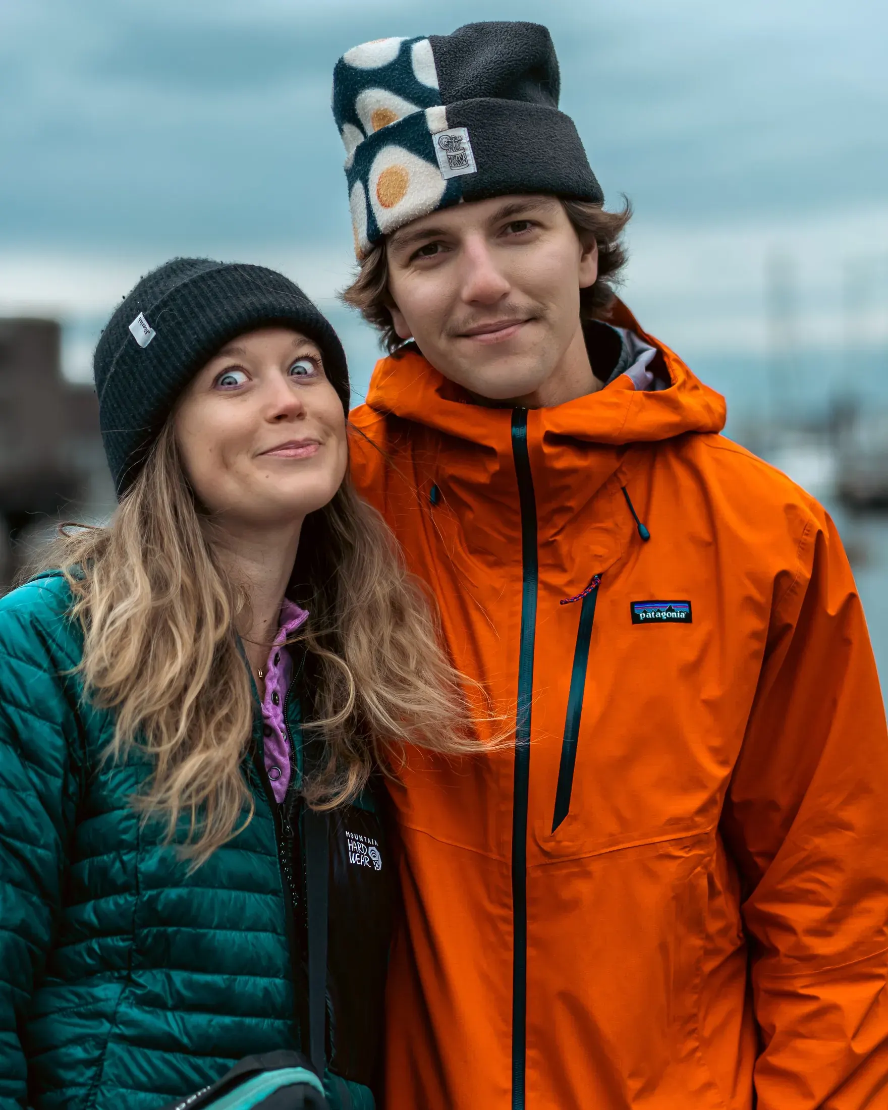 Couple in beanies and puffer jackets smiling close together